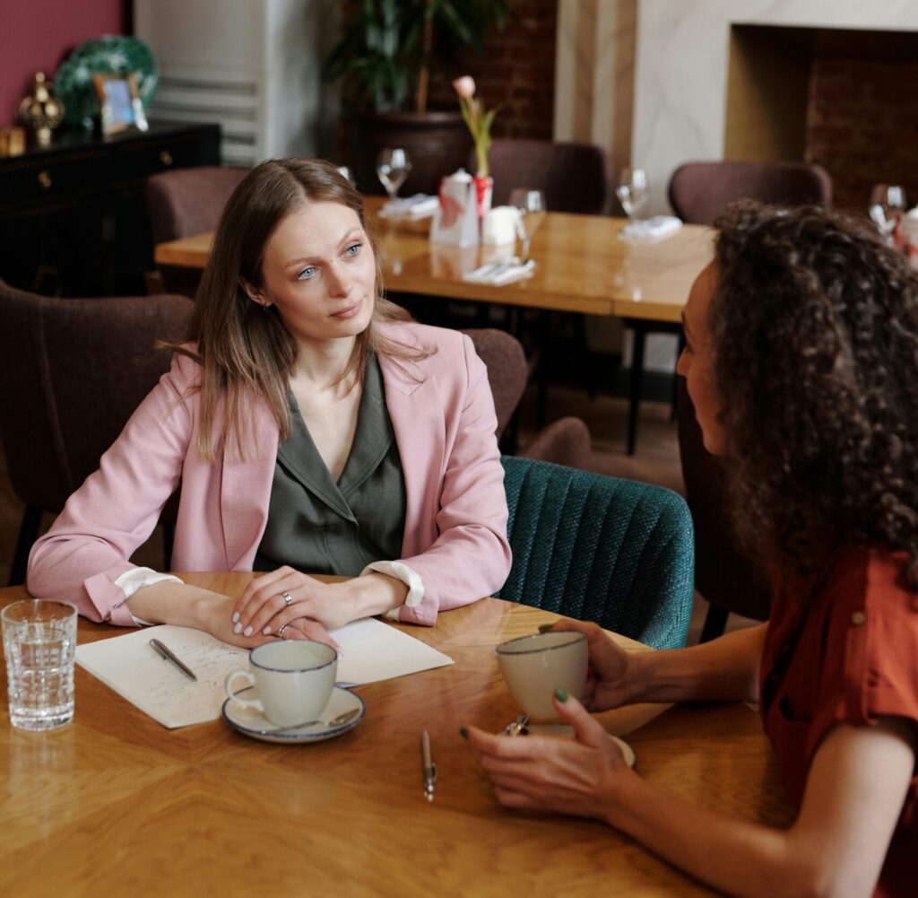 Two women having a thoughtful conversation in a cozy café setting, discussing over coffee.